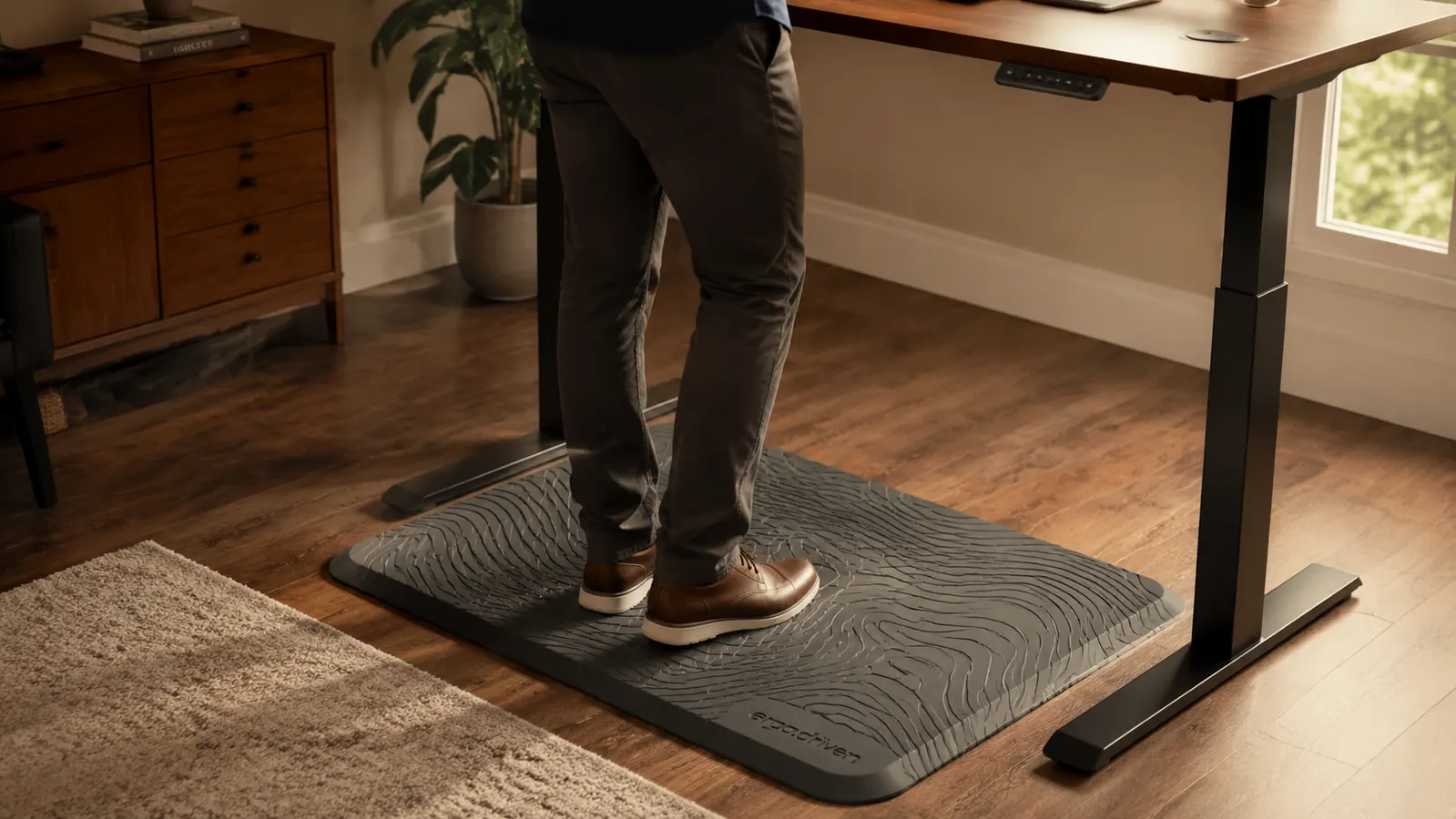 Person in socks standing on the Ergodriven Topo mat at a standing desk, foot resting on the raised center dome