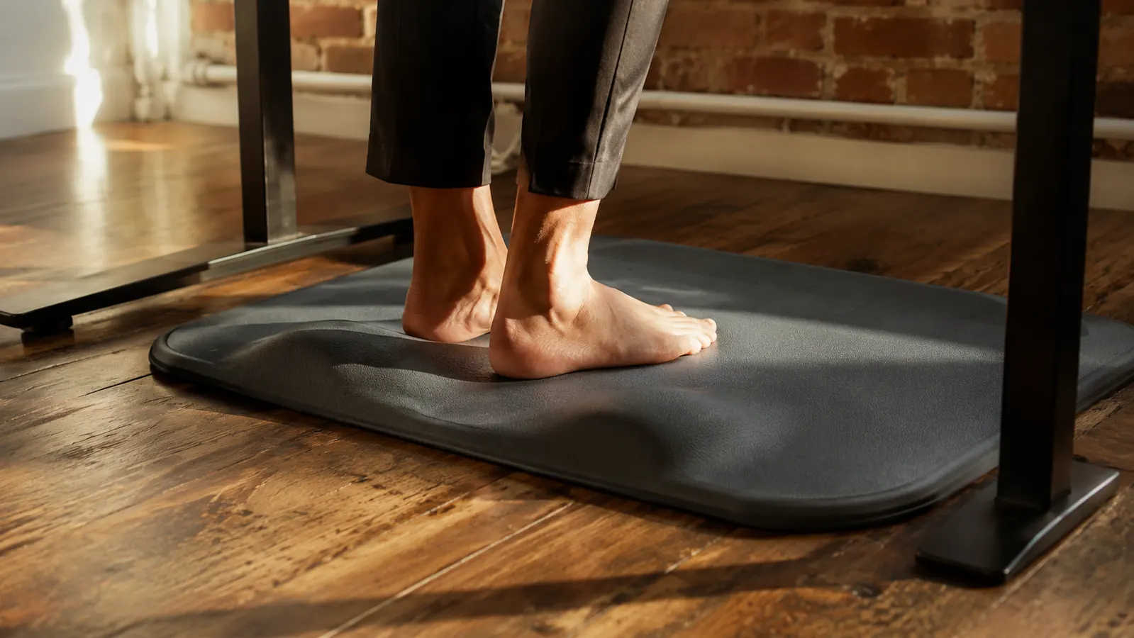 Person standing comfortably at a standing desk in a home office, relaxed posture, feet on an anti-fatigue mat