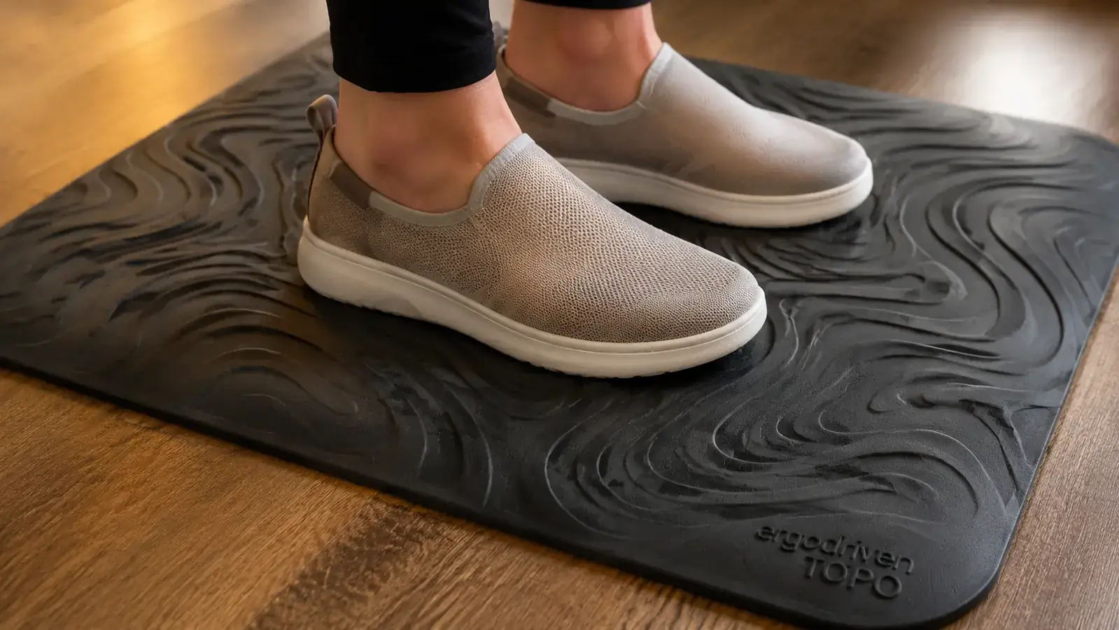 Close-up of feet on an Ergodriven Topo anti-fatigue mat showing the contoured terrain surface
