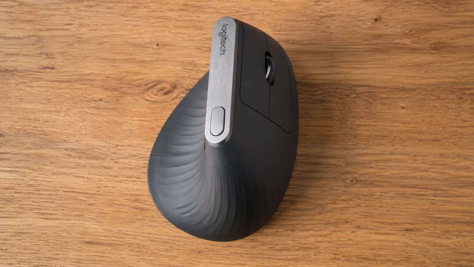 The Logitech MX Vertical mouse on a desk beside the Logitech Unifying receiver and USB-C charging cable