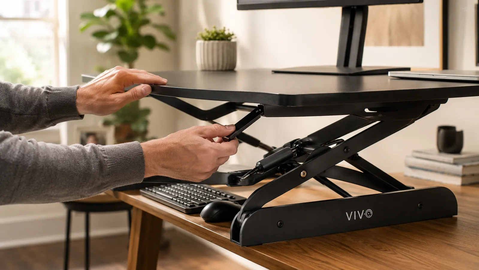 Hands lifting the VIVO desk converter platform upward using the squeeze handle, showing the spring mechanism in action from a front-angle view