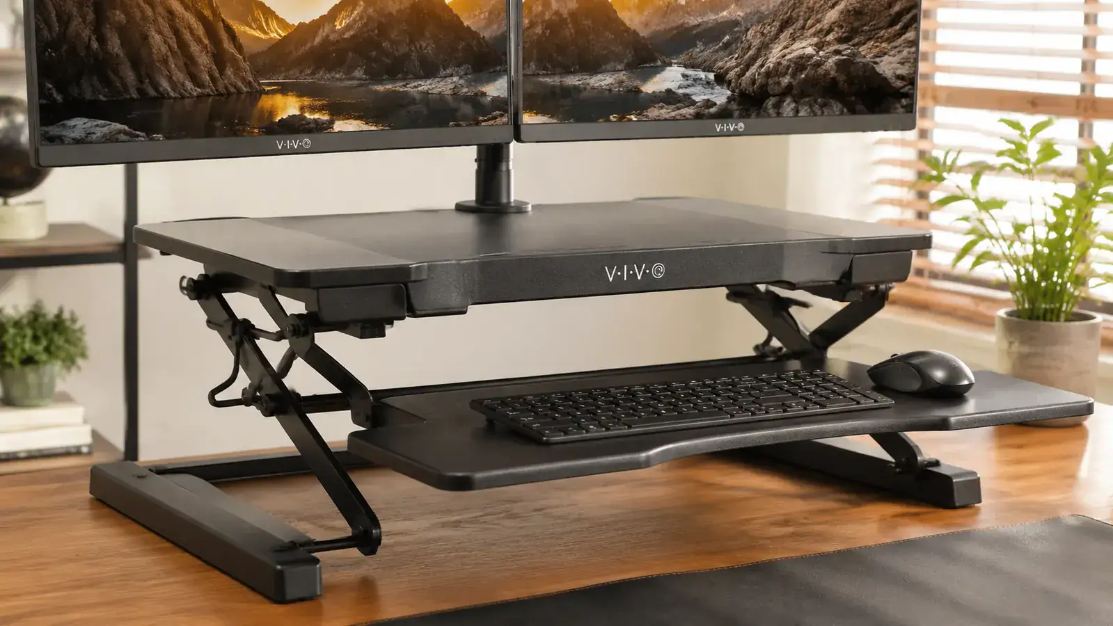 A person transitioning from sitting to standing at a desk converter by lifting the spring-loaded platform with one hand while keeping coffee mug on the desk
